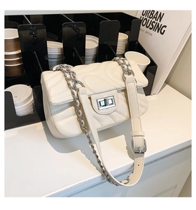 Detail of beige quilted crossbody bag with silver chain strap and metal turn-lock closure