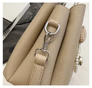 Detail of beige pebble texture bag featuring silver hooks and a pearl heart charm