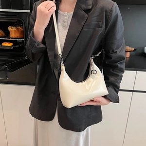 Détail du sac demi-lune crème avec logo embossé et pendentif sphérique argenté