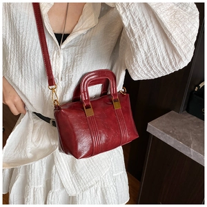 Detailed view of burgundy Boston bag with polished leather texture and gold hardware