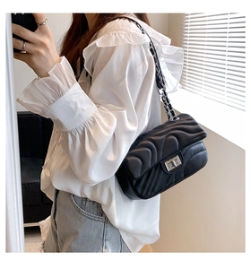 Close-up of black quilted shoulder bag with silver turn-lock and chain strap on model
