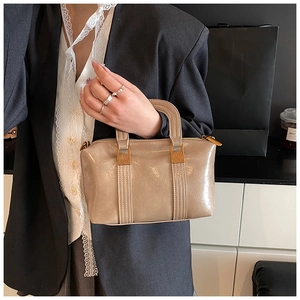 Detail of light brown patent leather handbag featuring golden metal hardware and top handle