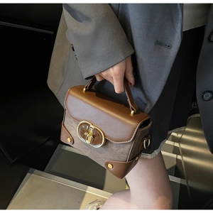 Detail of vintage brown box bag featuring a gold oval clasp and premium textured leather