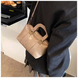 Detail of a beige leather crossbody bag with stitching and gold metal buckles