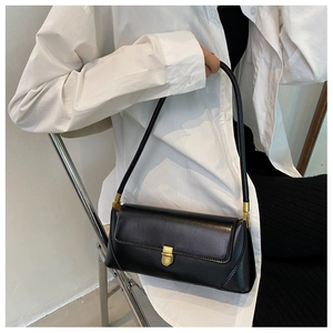 Close-up of minimalist black baguette bag with gold metal buckle on a white shirt background