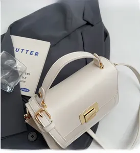 Detail of cream crossbody bag with gold rectangular buckle on grey fabric background