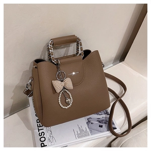 Detail of brown litchi leather handbag with silver chain handle and bow heart charm