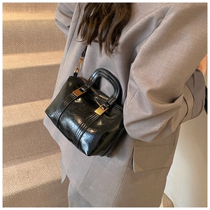 Close-up of black glossy patent leather Boston bag with gold zippers worn on a shoulder