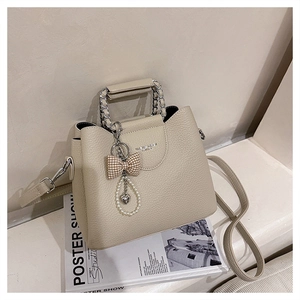Detail of cream crossbody bag featuring litchi grain texture and pearl heart charms
