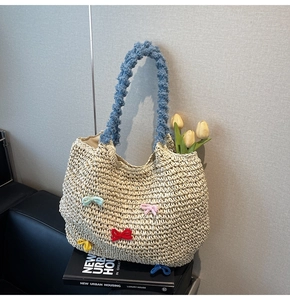 Detail of straw woven tote with colorful bows and blue plush handle on book stack
