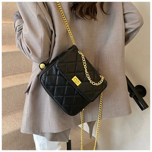 Détail d'un sac bandoulière matelassé noir avec chaîne dorée sur un blazer beige