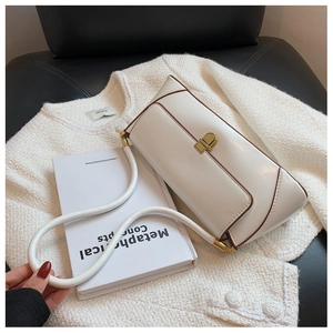 Detail of minimalist cream baguette bag with brown edge piping and gold twist lock clasp