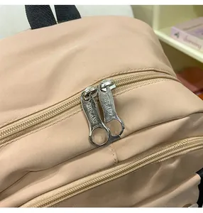 Detail of smooth metal double zippers with logo engraving on a khaki backpack