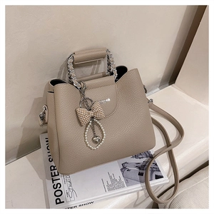 Close-up of beige lychee leather bucket bag with silver chain handle and pearl bow charm