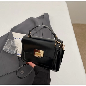 Detail of a sleek black leather crossbody bag featuring a classic gold square metal clasp