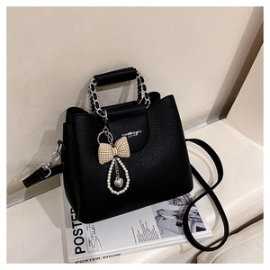 Detail of black lychee grain leather tote bag with metal chain handle and pearl charm
