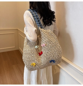 Detail of straw woven tote bag featuring colorful crochet bows and denim shoulder strap