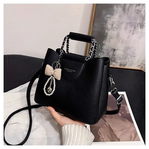 Detail of black litchi texture handbag with pearl bow charm and metal chain handle