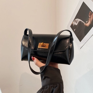 Sac sous le bras noir brillant avec fermoir doré dans un décor minimaliste chic