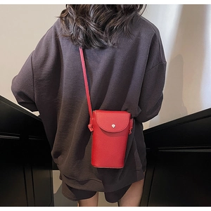 Detail of red pebbled leather crossbody phone bag with silver buckle worn by a model