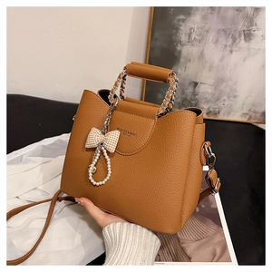 Close-up of caramel brown tote bag featuring pearl pendant and leather metal chain handle