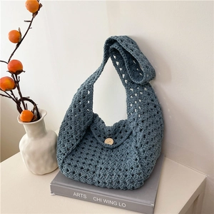 Minimalist woven bucket bag in blue with mesh texture and wooden button on a display book