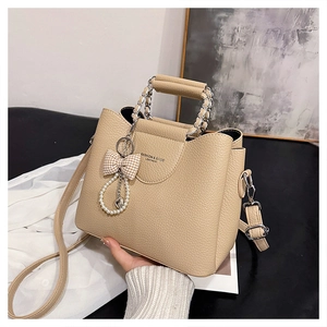 Detail of beige lychee leather handbag with chain handle and pearl bow charm