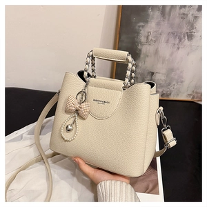 Detail of warm beige litchi leather bag with chain handle and pearl bow pendant decoration