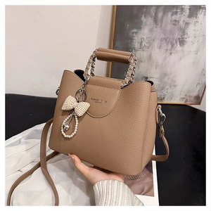 Detail of taupe leather handbag featuring a pearl bow charm and chain handle strap