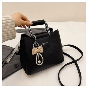 Detail of black lychee grain leather tote with silver chain, pearl heart and bow charm