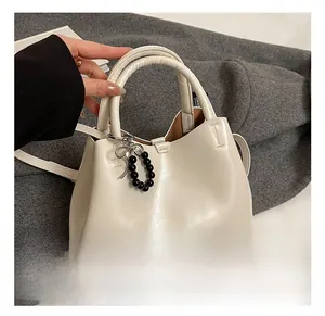 Close-up of cream PU leather tote bag with black beaded bow charm and shoulder strap