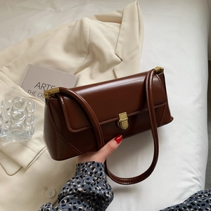 Brown retro leather baguette bag with a gold metal clasp shown in a lifestyle setting