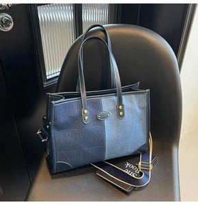 Dettaglio borsa tote in denim a contrasto con cuciture bianche e tracolla a righe su sedia