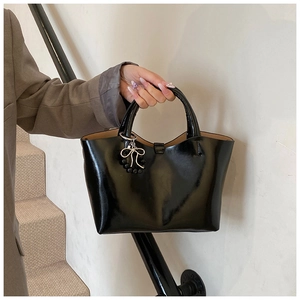 Close-up of black glossy tote bag with stylish bead and bow pendant on textured leather