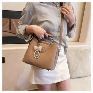 Detail of brown litchi leather bag with chain handle and pearl bow charm accessory