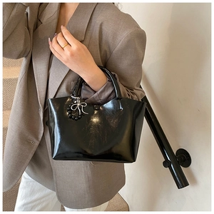 Close-up of black glossy handbag with silver bow and beads on stylish lady in brown suit