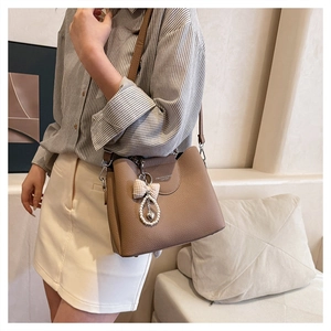 Close-up of tan lychee leather handbag featuring a pearl bow charm and logo detail