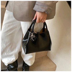 Detail of glossy black patent leather tote bag with elegant silver bow pendant