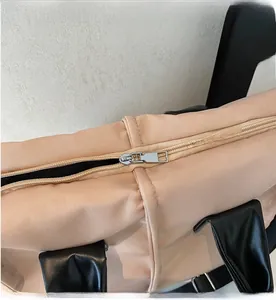 Close-up of smooth metal zipper and black leather handles on beige nylon handbag
