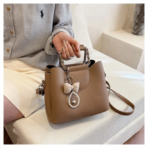 Detail of brown litchi leather bag with chain handle, pearl charms and bow accessory