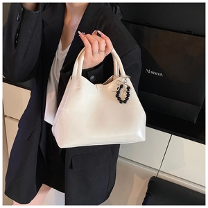 White glossy tote bag with black beaded bow charm shown on model in a sleek minimal style