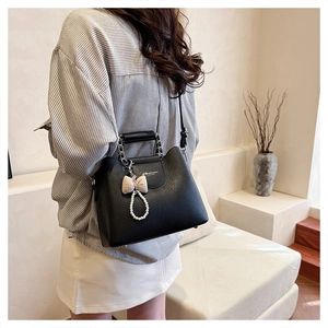 Detail of black lychee leather bag with silver chain handle and pearl bow charm