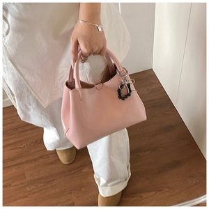 Pale pink leather tote bag with black bead bow charm held by model indoors