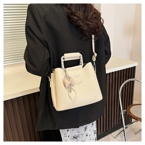 Detail of off-white lychee grain leather bag with chic bow and pearl pendant decoration
