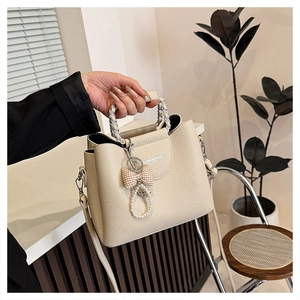 Detail of cream white leather bag with chain handle and pearl bow charm accessory