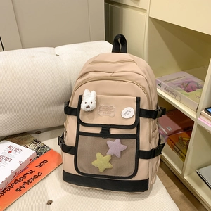 Cute beige nylon backpack with plush bunny accessory on a cozy striped sofa