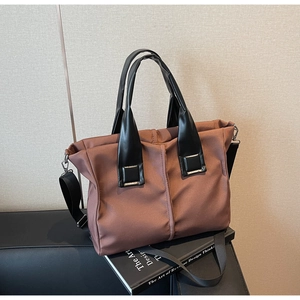 Detailed view of brown fabric handbag with black leather handles on a decorative book