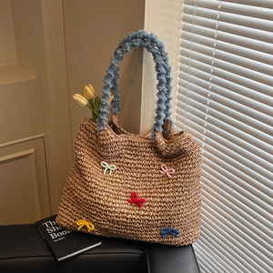 Handwoven straw tote bag with colorful bows and blue velvet handles in a sunny setting
