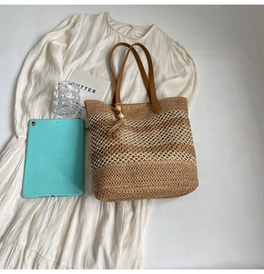 Detail of woven straw tote bag with brown leather handles and decorative wood bead tassels