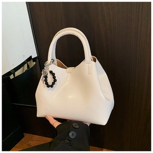 Detail of a creamy white bucket handbag with black beaded charm and bow decoration
